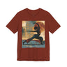 A rust colored short-sleeve crewneck t-shirt featuring a Black woman in a yoga pose against a warm, abstract sunset background.