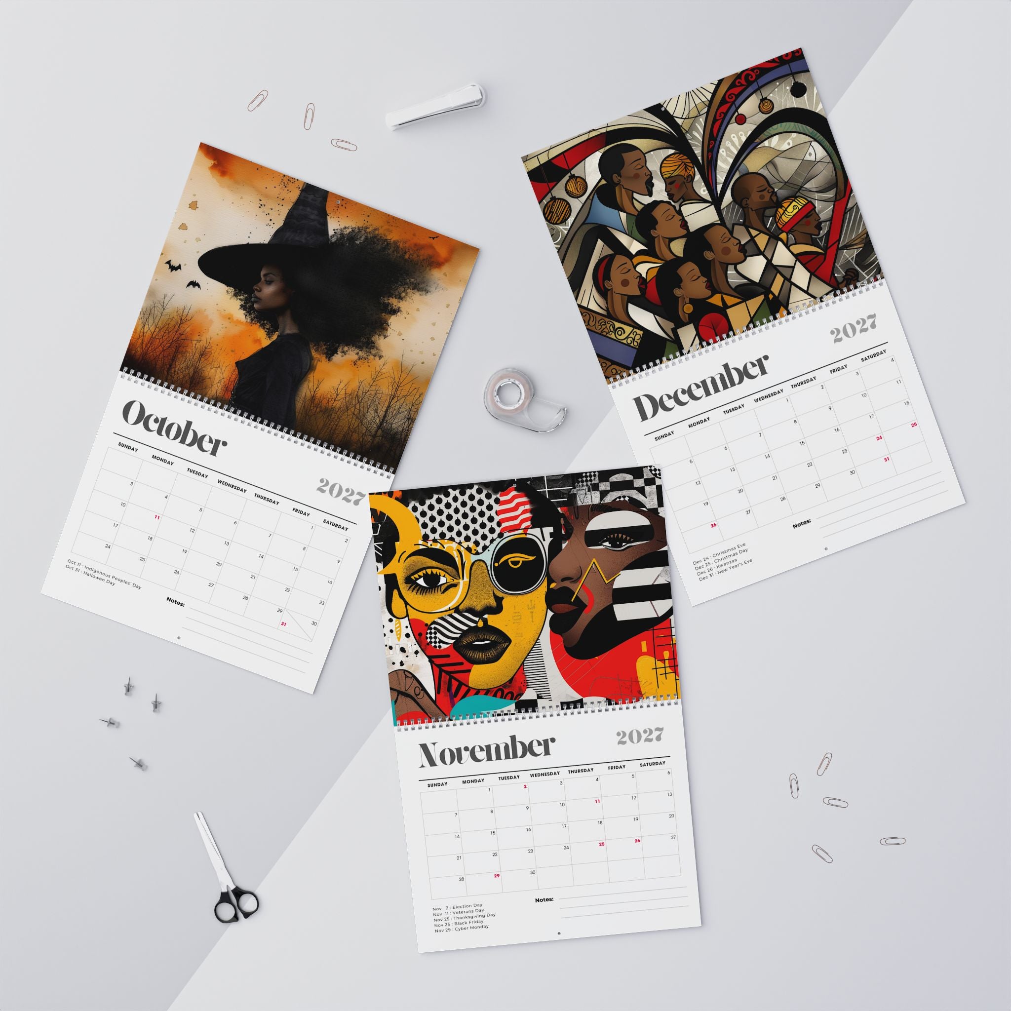 Three spiral-bound Afrocentric Abstract calendars for October, November and December 2027 are arranged on a light gray surface with art portraits printed on the pages. The calendars feature colorful abstract and portrait illustrations, with the months and years printed on white page layouts.
