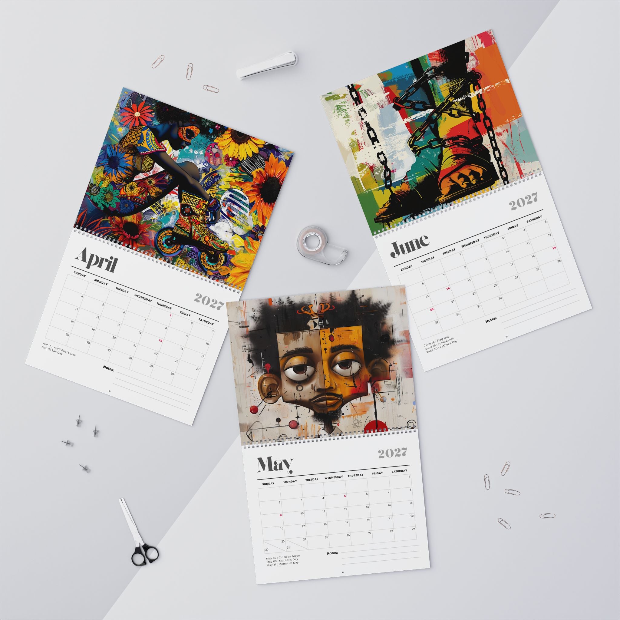 Three spiral-bound Afrocentric Abstract calendars for April, May and June 2027 are arranged on a light gray surface with art portraits printed on the pages. The calendars feature colorful abstract and portrait illustrations, with the months and years printed on white page layouts.