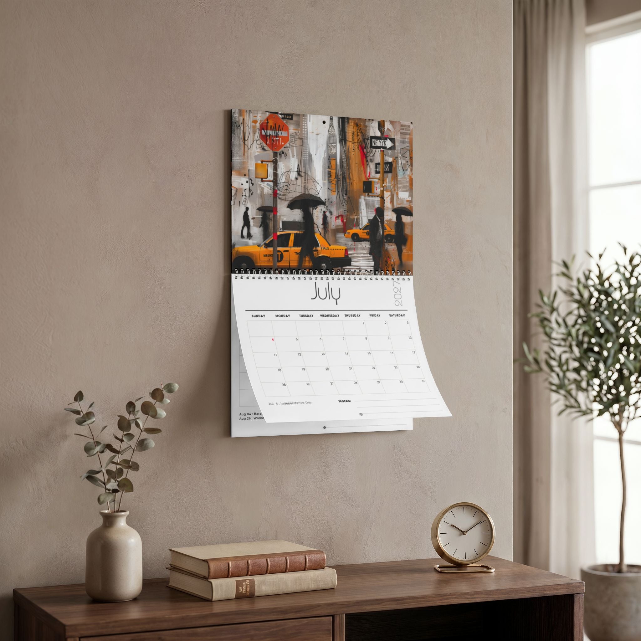 A spiral-bound wall calendar featuring a Manhattan city street scene with yellow taxis and umbrellas, hanging on a beige wall above a wooden console table with books, a vase, and a small clock. Size 11" x 8.5"