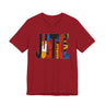 A red short-sleeve crewneck t-shirt featuring a large graphic on the chest spelling 'JUSTICE' in bold, multi-colored abstract shapes, shown against a plain white background.