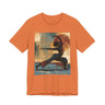 A burnt orange colored short-sleeve crewneck t-shirt featuring a Black woman in a yoga pose against a warm, abstract sunset background.