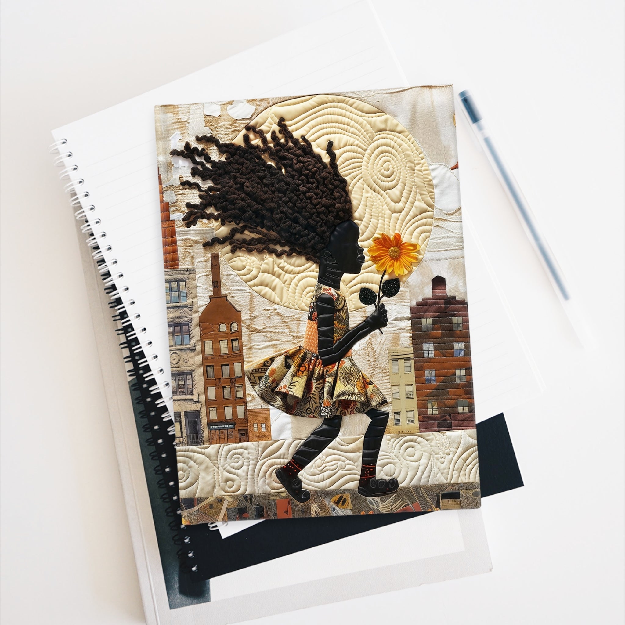 Hardcover journal featuring on the cover, a young Black girl carrying a yellow sunflower as she walks through the historic streets of Harlem lays on top of various notebooks against a white background.