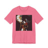 A pink short-sleeve crewneck t-shirt featuring a square graphic print of an artistic portrait of a Black woman with high-cropped hair, gold hoop earrings, and red lipstick on a dark background.