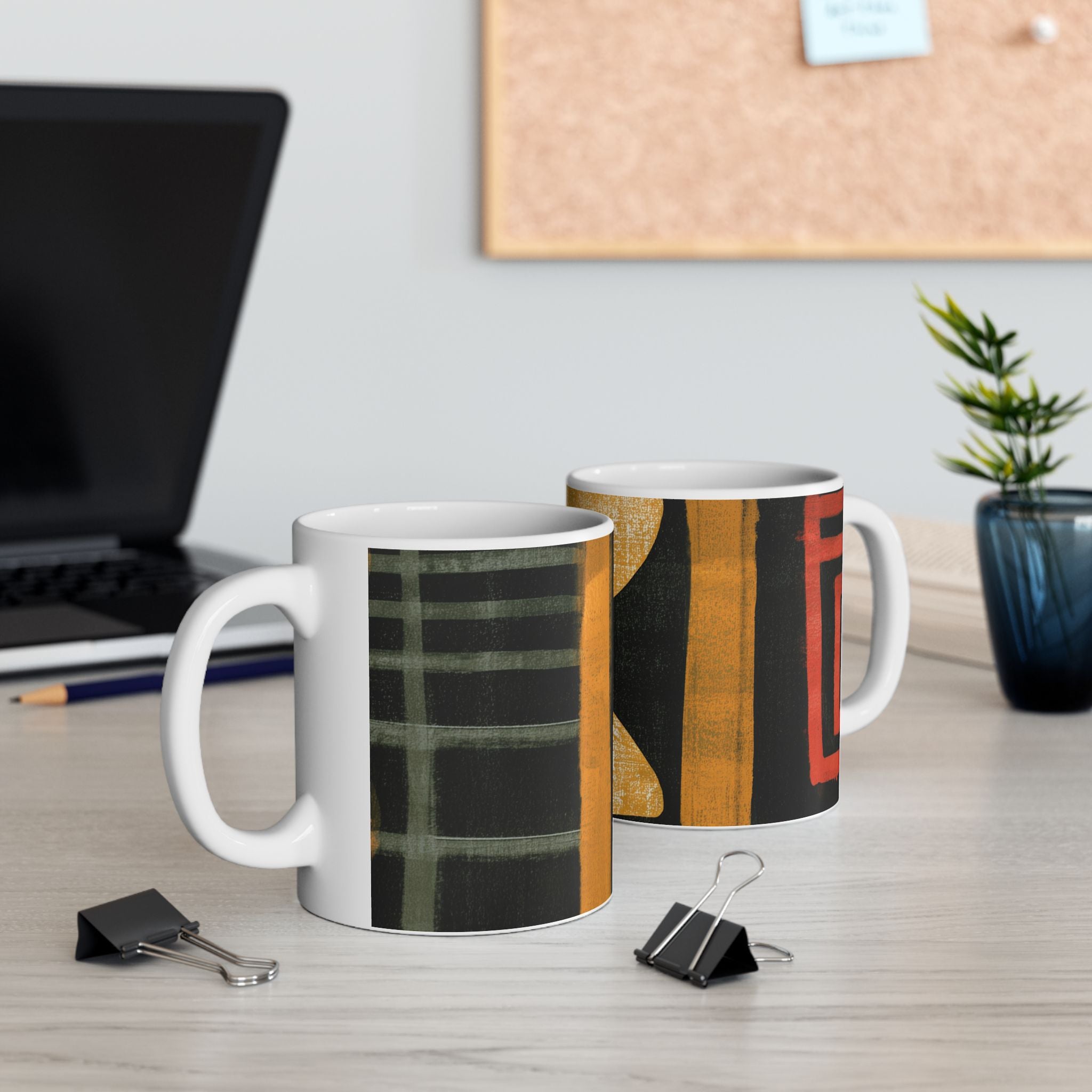 Left and right handle views of 11 oz. red, black, gold and cream abstract art coffee mug featuring bold geometric circles, stripes, organic shapes and a Bauhaus-inspired modern design, displayed on top of an office desk with a laptop computer in the background.