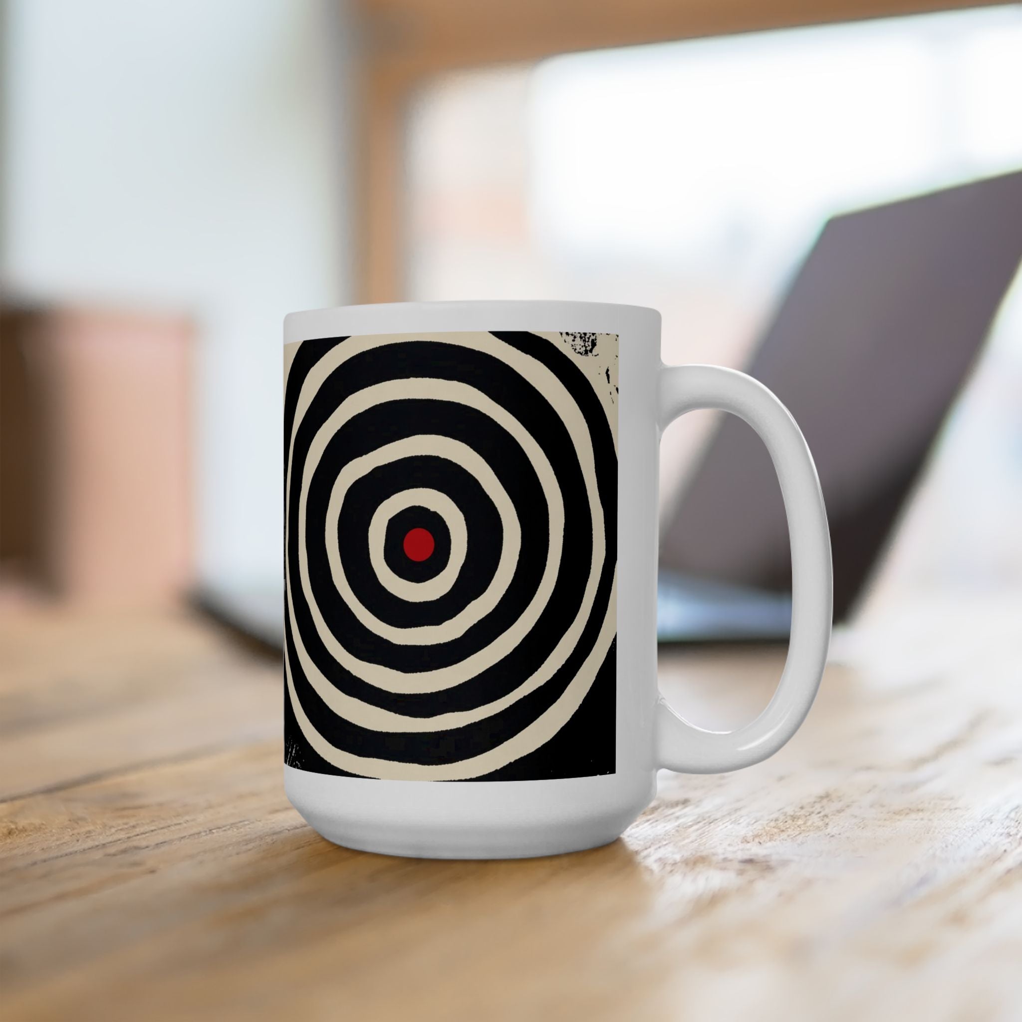 Right handle views of 15 oz. red, black and cream abstract art coffee mug featuring bold geometric circles, stripes, organic shapes and a Bauhaus-inspired modern design, displayed on top of an office desk with a laptop computer in the background.