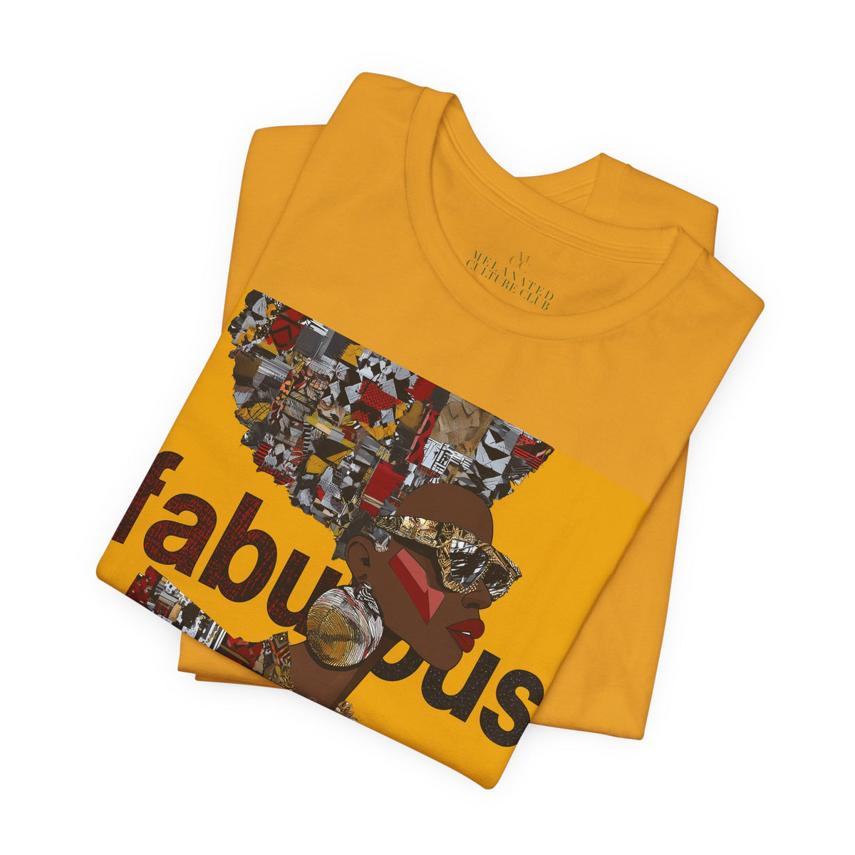 A folded mustard yellow short-sleeve t-shirt featuring an Afrocentric Black woman with a large graphic print on the front with the word 'fabulous' in dark brown text over a collage of colorful objects.