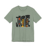 A sage green short-sleeve crewneck t-shirt featuring a graphic print of the word 'JUSTICE' filled with stylized illustrations of African American faces in black, brown, and orange tones.