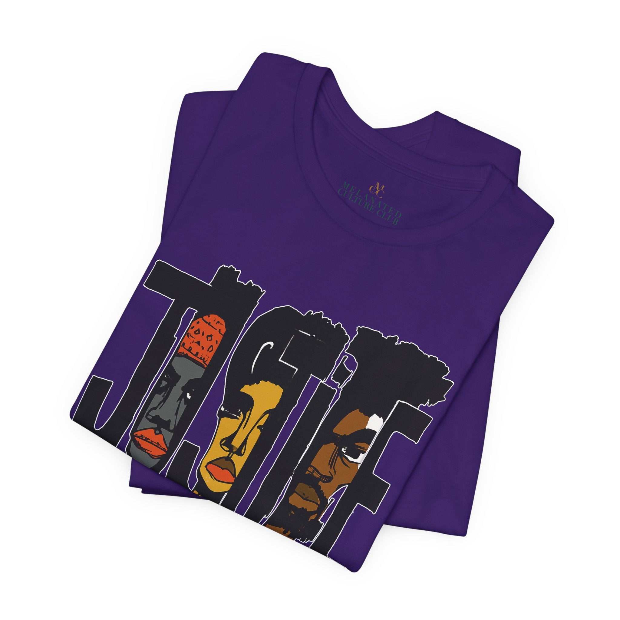 A folded purple short-sleeve crewneck t-shirt featuring a graphic print of the word 'JUSTICE' filled with stylized illustrations of African American faces in black, brown, and orange tones.