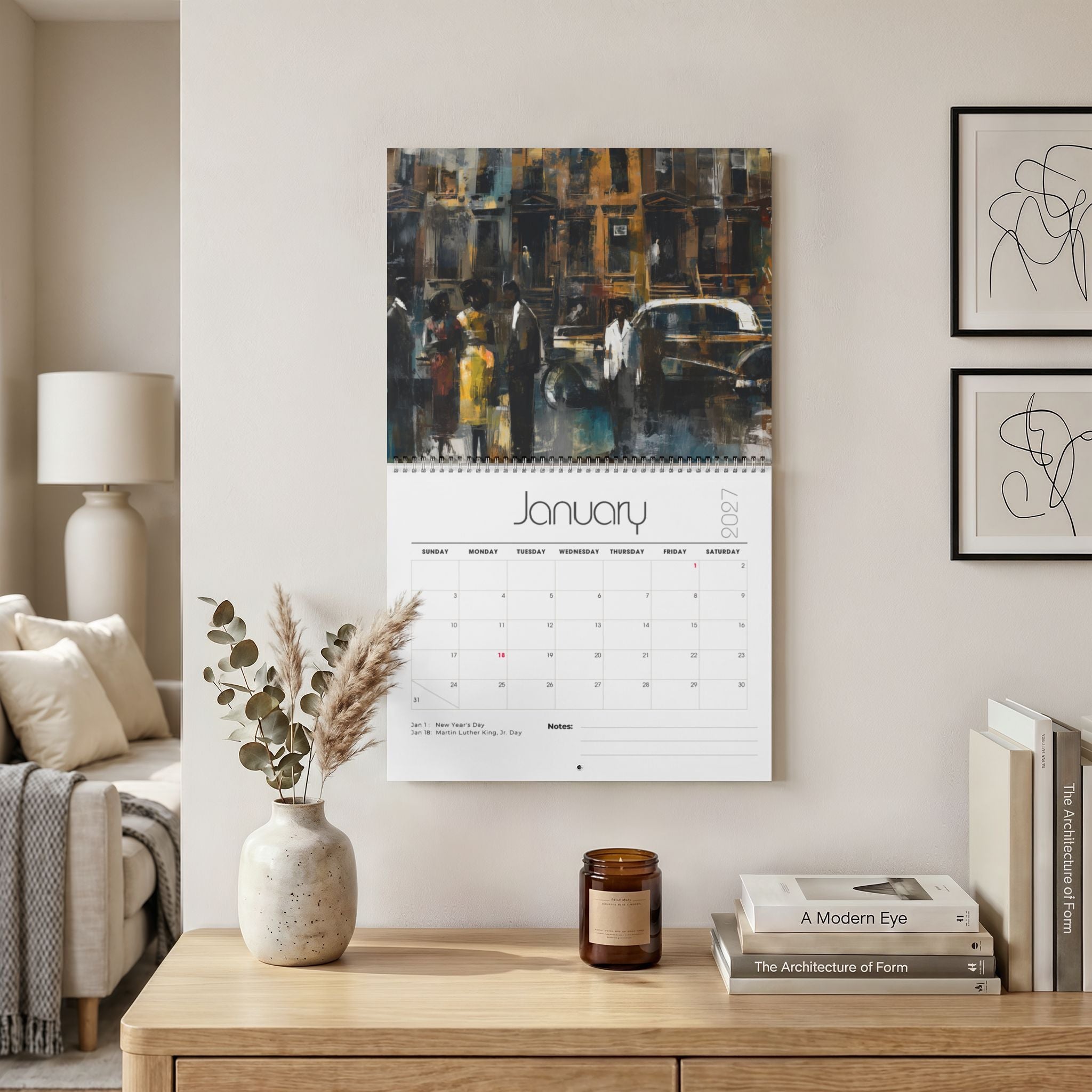 A wall-mounted calendar hanging in a styled living room, with a painting of vintage Harlem street scene across the top and a white January 2027 page below. The room includes a wooden console table, books, a candle, a vase with dried grasses, and framed wall art. Size 14" x 11.5"