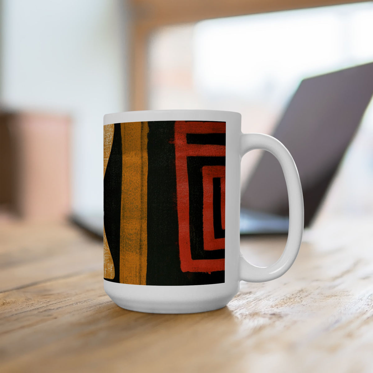 Right handle views of 15 oz. red, black, gold and cream abstract art coffee mug featuring bold geometric circles, stripes, organic shapes and a Bauhaus-inspired modern design, displayed on top of an office desk with a laptop computer in the background.
