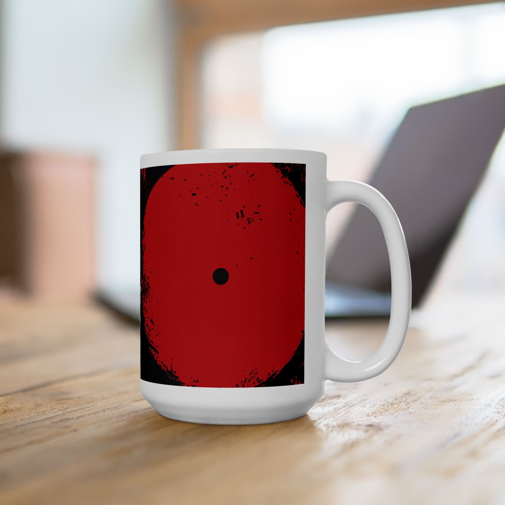 Right handle views of 15 oz. red, black and cream abstract art coffee mug featuring bold geometric circles, stripes, organic shapes and a Bauhaus-inspired modern design, displayed on top of an office desk with a laptop computer in the background.