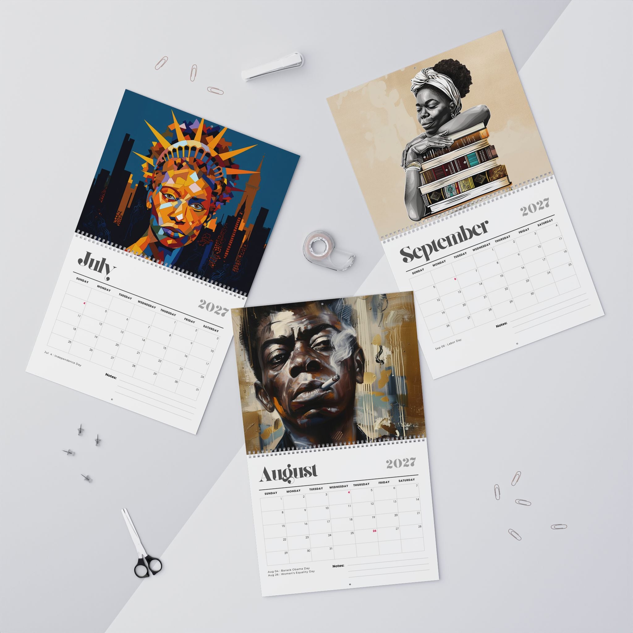 Three spiral-bound Afrocentric Abstract calendars for July, August and September 2027 are arranged on a light gray surface with art portraits printed on the pages. The calendars feature colorful abstract and portrait illustrations, with the months and years printed on white page layouts.