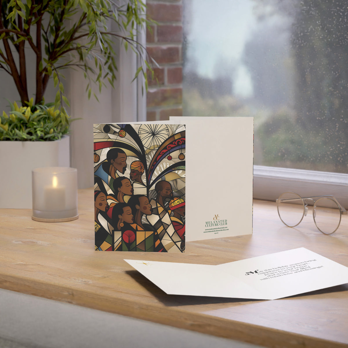 African American Christmas card featuring a joyful Black choir in an artistic stained glass-inspired design, placed on top of a oak desktop with window in the background.