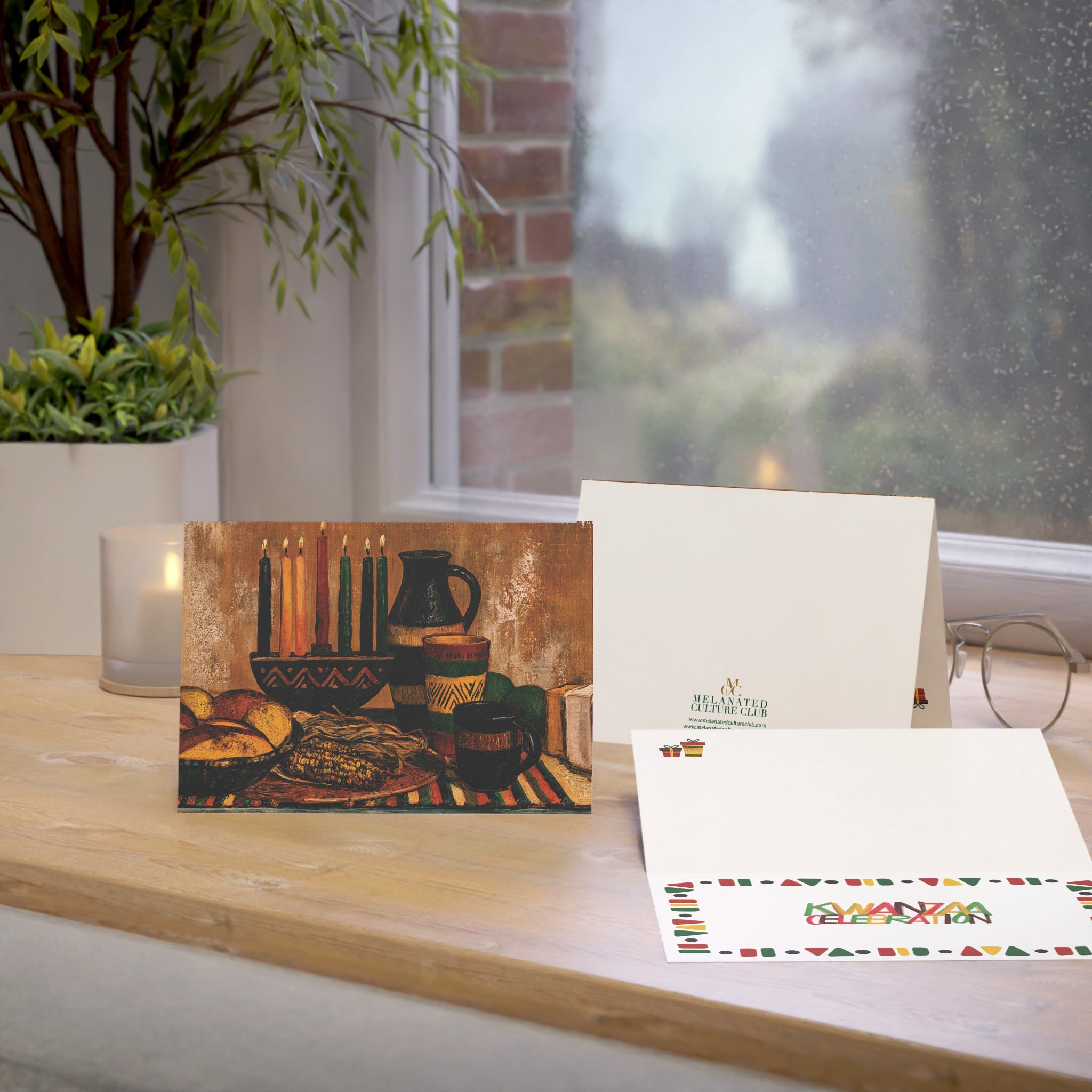 An Afrocentric Kwanzaa holiday greeting card celebrating Black heritage, African American culture, family, unity, community, and the Seven Principles of Kwanzaa, placed on a oak table with a window in the background.