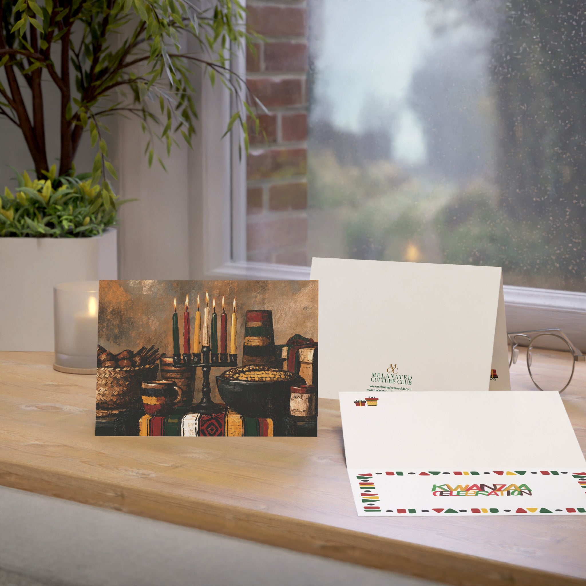 An Afrocentric Kwanzaa holiday greeting card celebrating Black heritage, African American culture, family, unity, community, and the Seven Principles of Kwanzaa, placed on a oak table with a window in the background.