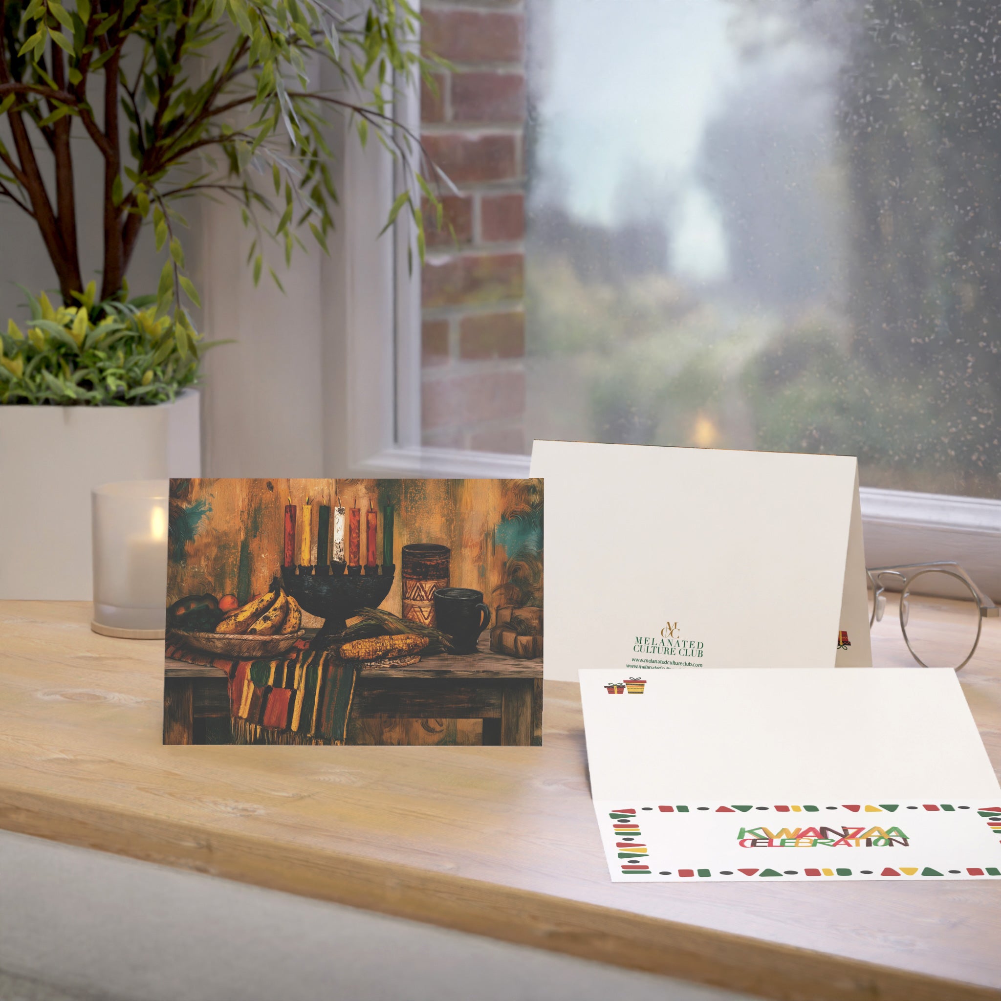 An Afrocentric Kwanzaa holiday greeting card celebrating Black heritage, African American culture, family, unity, community, and the Seven Principles of Kwanzaa, placed on a oak table with a window in the background.