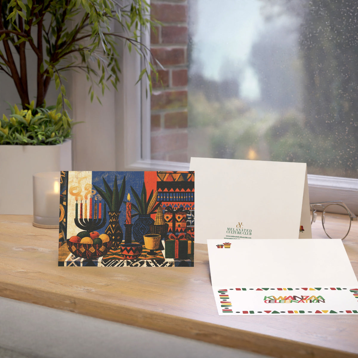 An Afrocentric Kwanzaa holiday greeting card celebrating Black heritage, African American culture, family, unity, community, and the Seven Principles of Kwanzaa, placed on a oak table with a window in the background.