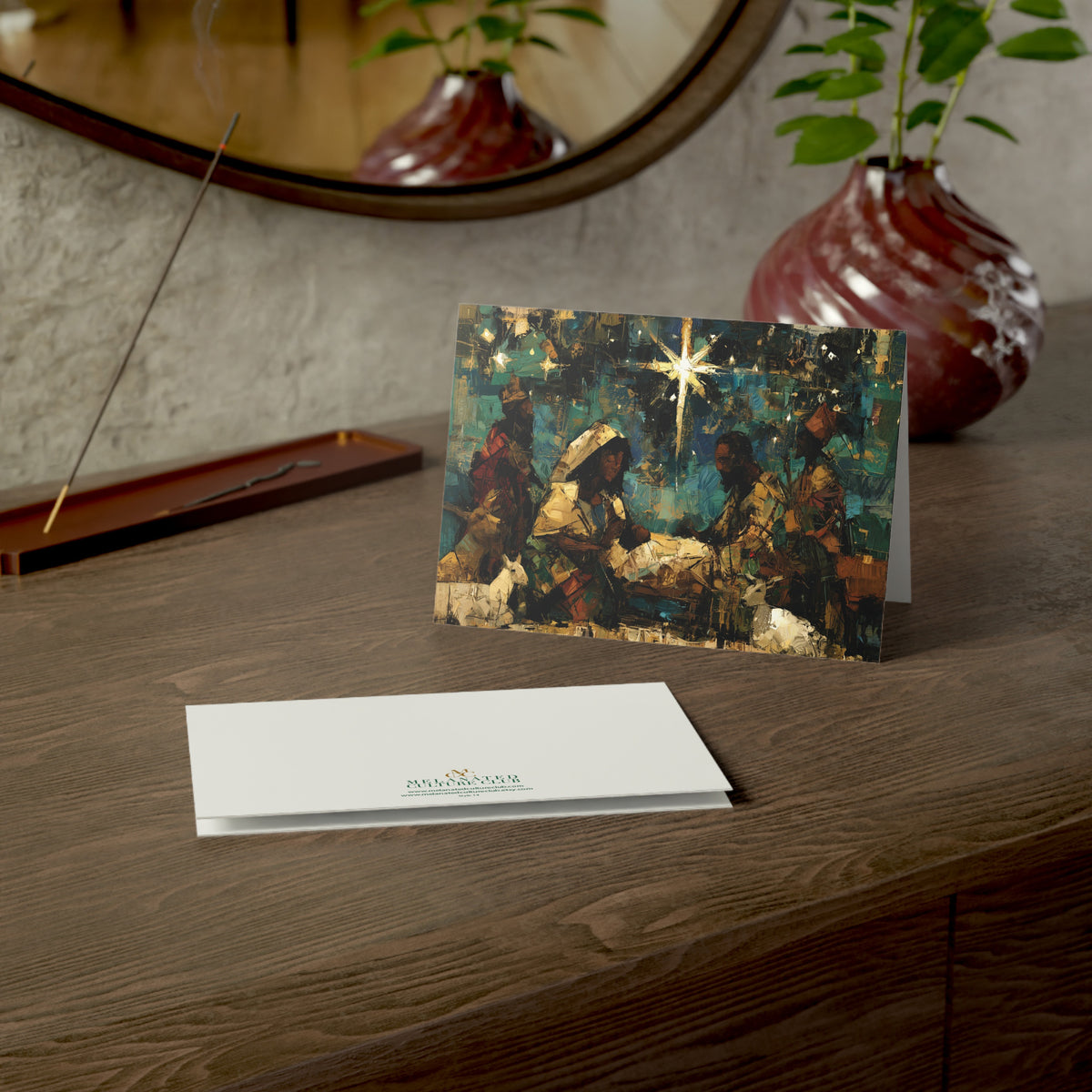 A Christmas greeting card featuring a colorful, stylized nativity scene with Black Baby Jesus, Mary, Joseph, Wise men and barn animals with a bright star in the night sky, on top of a wood surface.