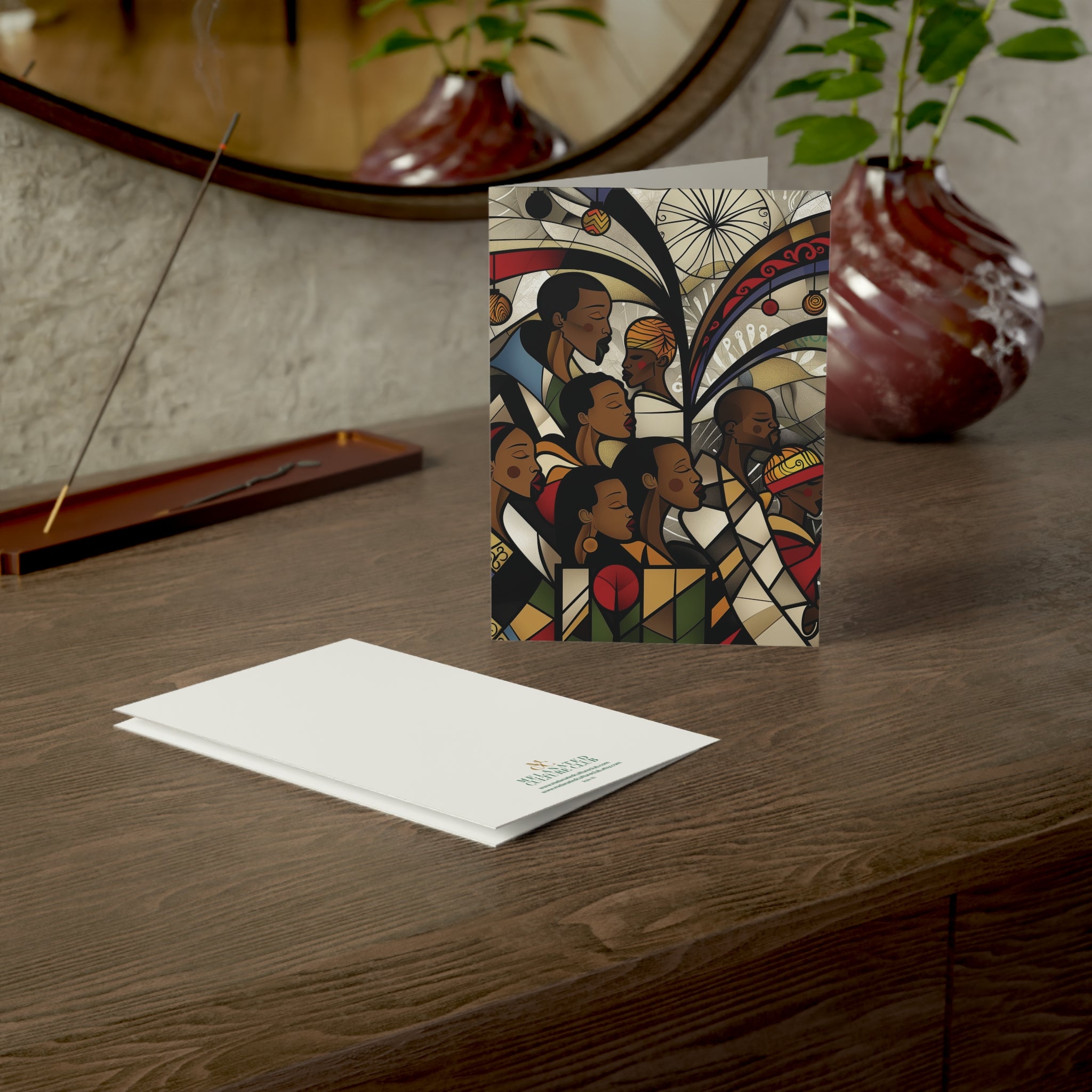 African American Christmas cards featuring a joyful Black choir in an artistic stained glass-inspired design, placed on top of a wood cabinet, with back view of card showing brand logo. 
