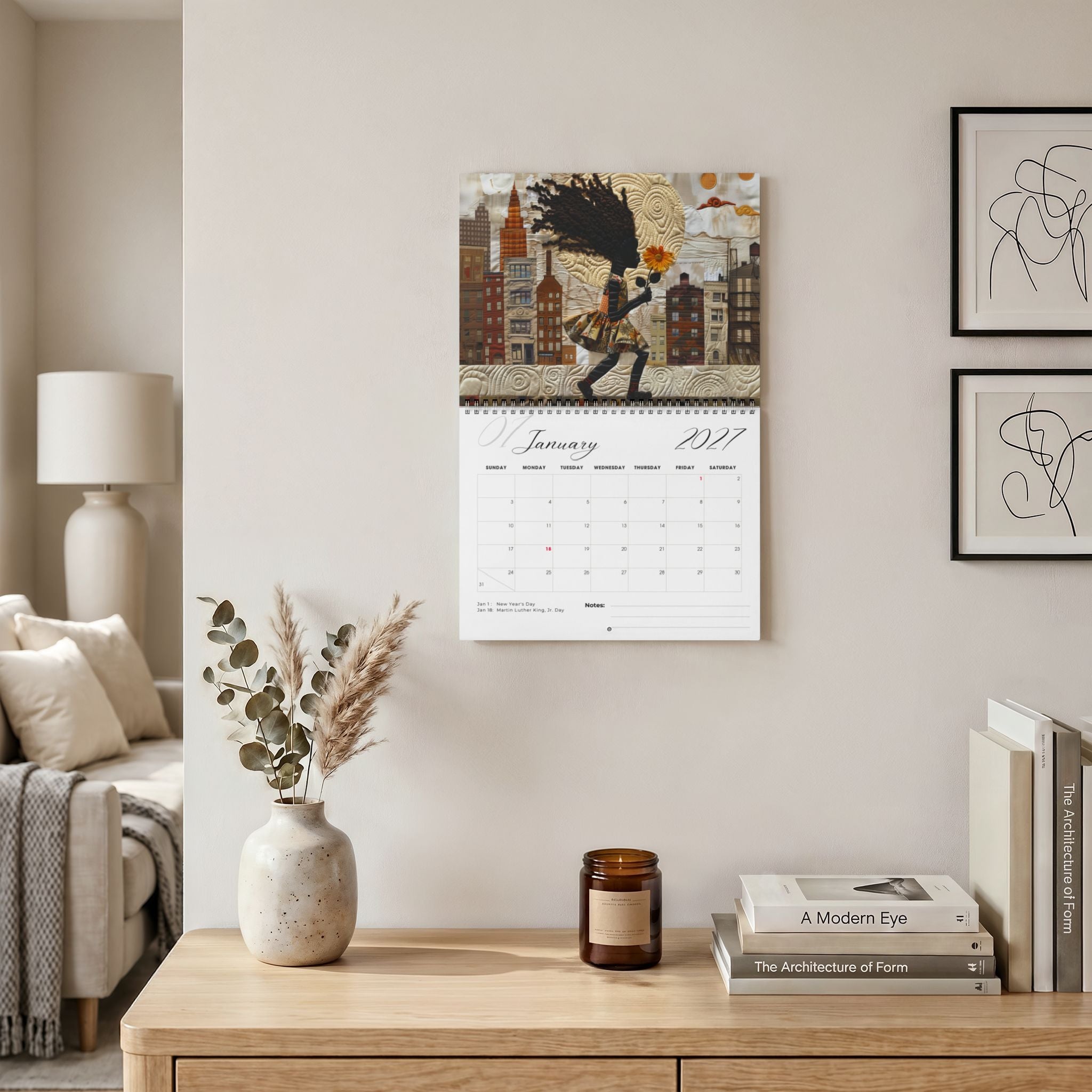 The Rooted in Home 2027 wall-mounted calendar hangs above a wooden console table in a styled living room. Size version 11" x 8.5".