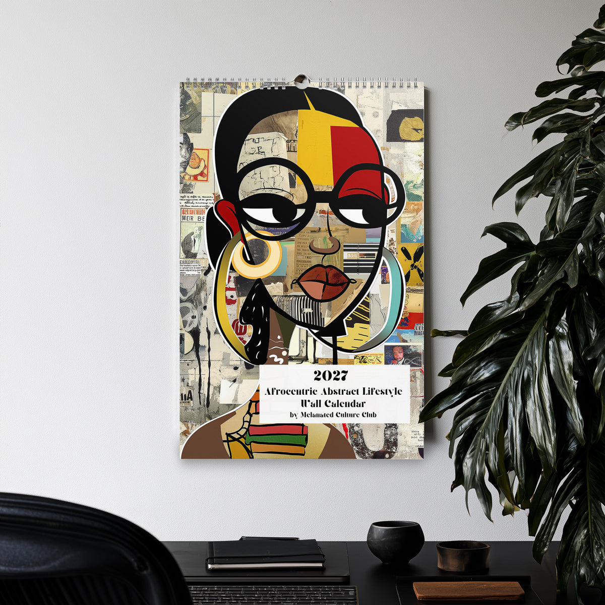 Front cover views of an 11" x 17" 2027 Afrocentric abstract wall calendar featuring colorful African American artwork inspired by Afrofuturism, graffiti art, urban culture, bold textures, and contemporary Black artistic expression.  Displayed hanging on a wall in an office setting with a large green plant.