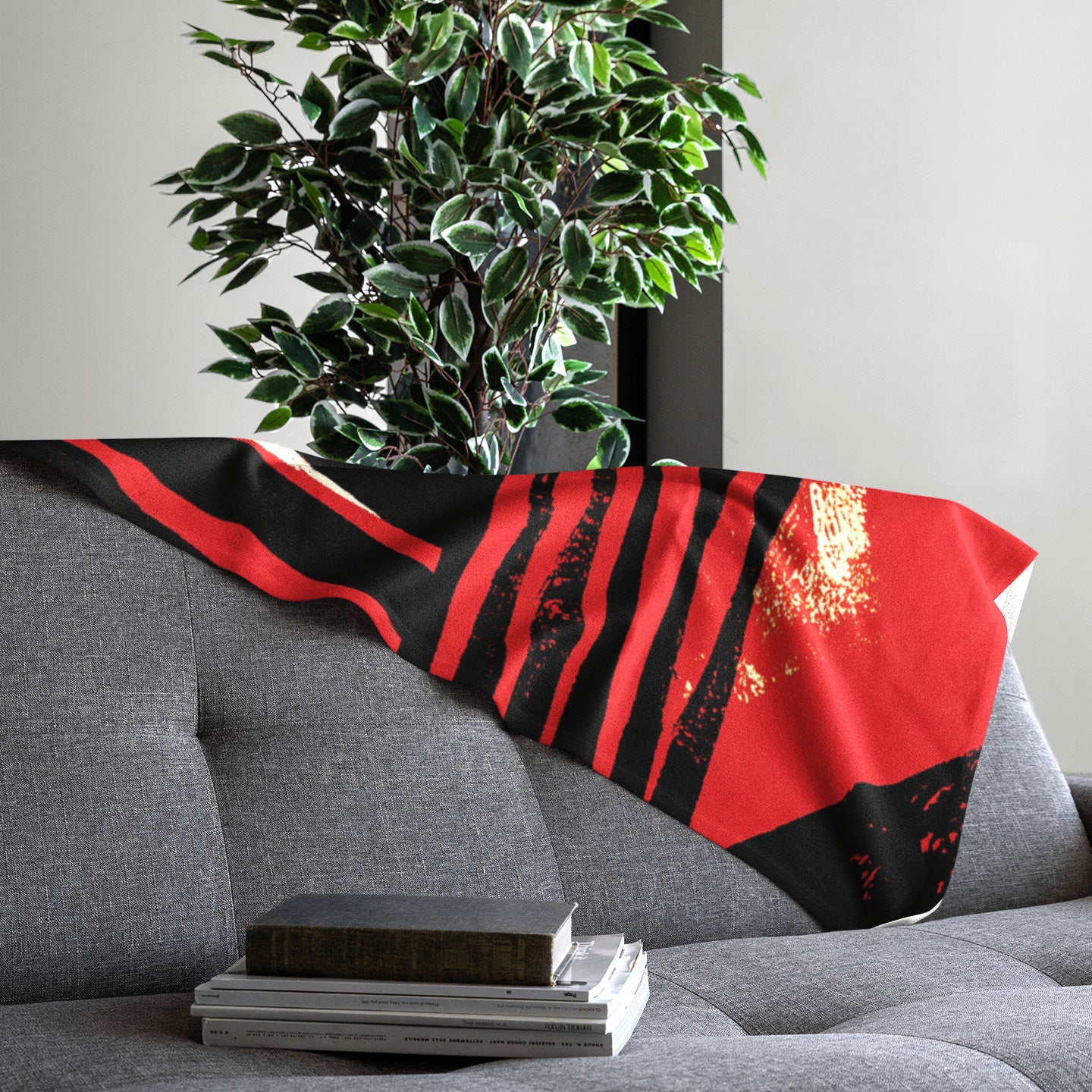 Spread out view of Afrocentric geometric art throw blanket featuring bold black, red, gold, cream, and neutral abstract patterns with circles, spirals, grids, and textured African-inspired geometric shapes, draped over the back of a grey sofa.