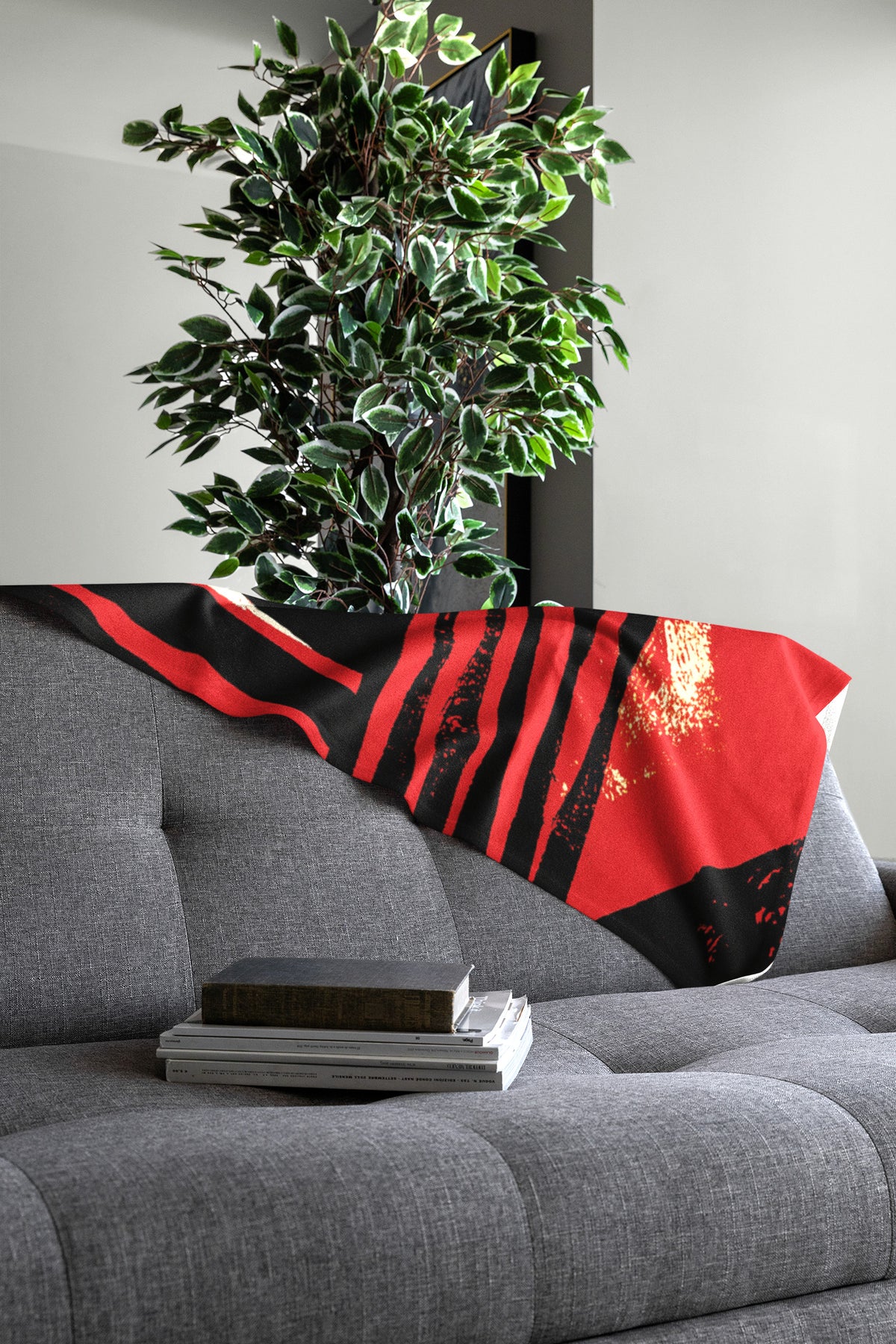 Spread out view of Afrocentric geometric art throw blanket featuring bold black, red, gold, cream, and neutral abstract patterns with circles, spirals, grids, and textured African-inspired geometric shapes, draped over the back of a grey sofa.