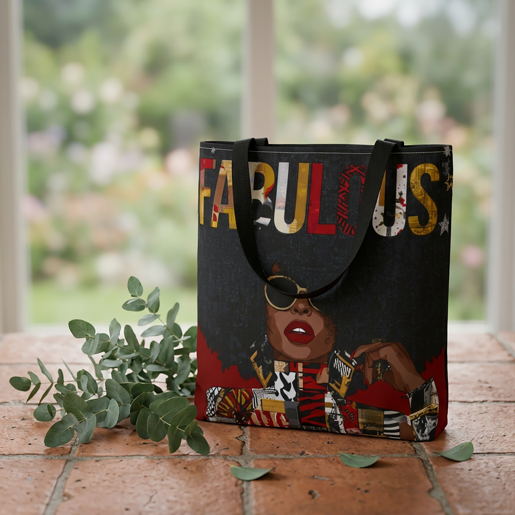 Fabulous Black woman tote bag featuring an abstract Afrocentric female portrait in colorful pop art and graffiti style with the word Fabulous in large graphic letters, sitting on top of cement block table with eucalyptus leaves.