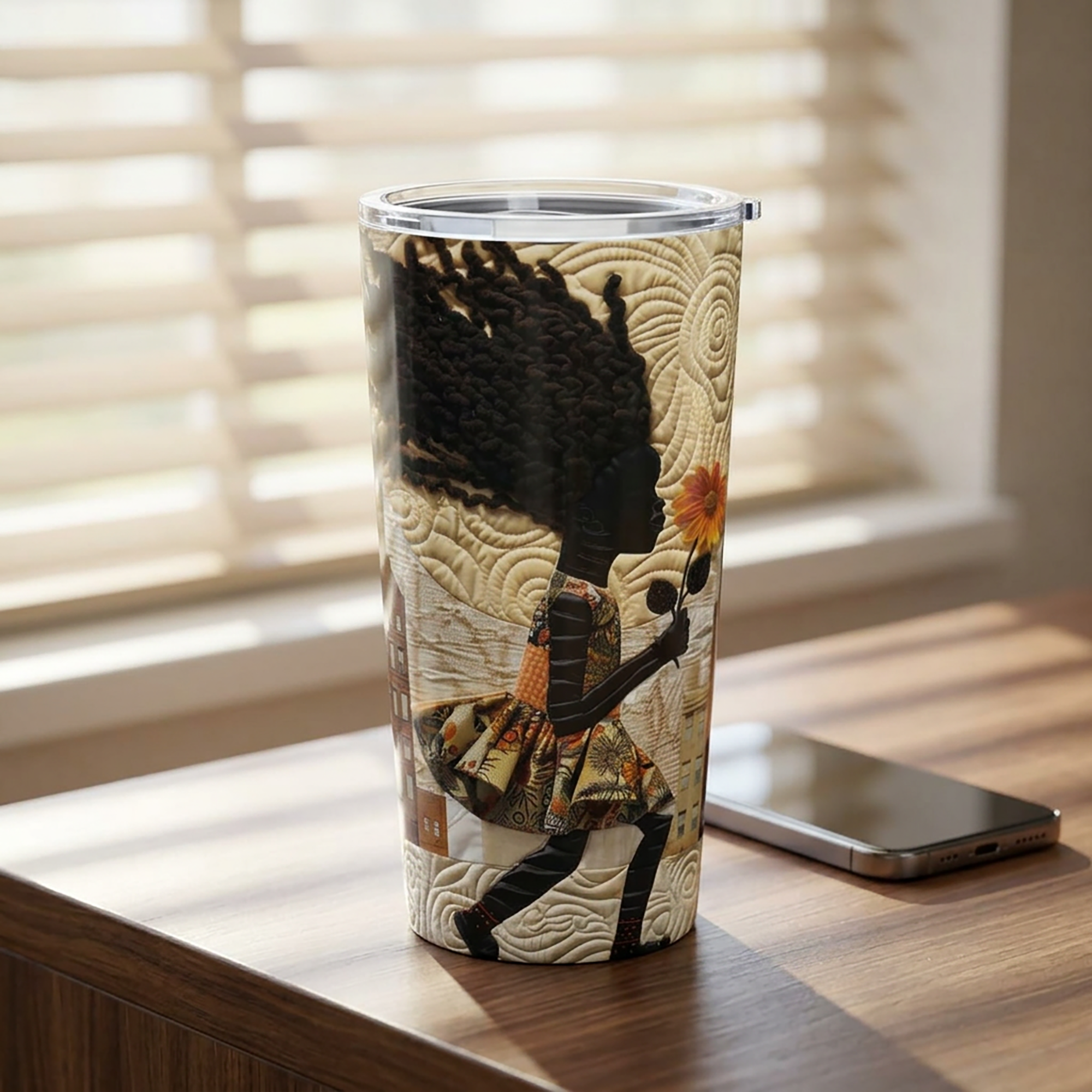 20 oz stainless steel travel tumbler featuring a young Black girl carrying a yellow sunflower while walking through Harlem. Her long braids blow in the wind with historic Harlem brownstones and New York City architecture in the background, illustrated in a colorful Afrocentric faux quilt collage style.  Tumbler is featured on a wood desktop with a smartphone.