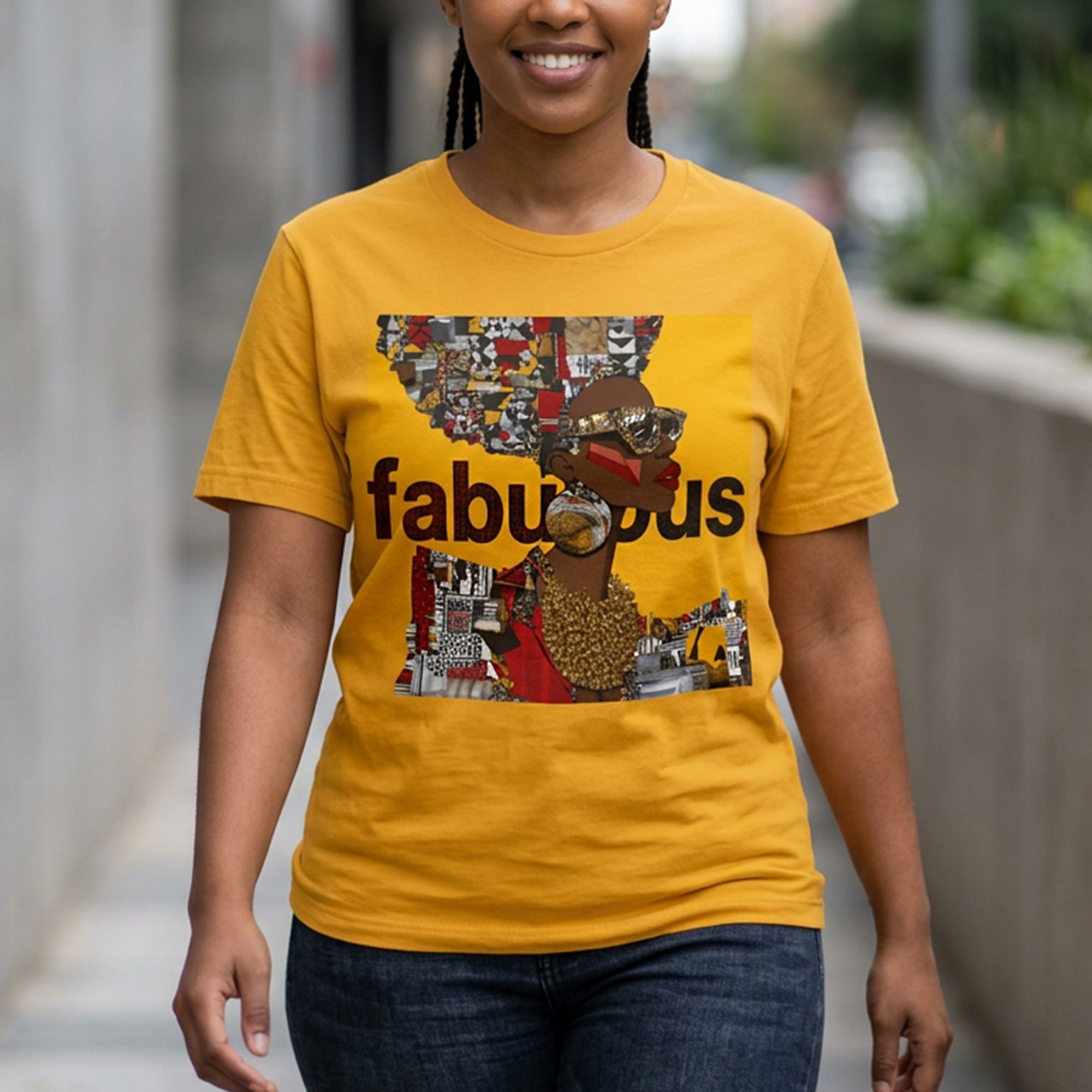 A woman wearing a mustard yellow graphic t-shirt with a collage-style print featuring an Afrocentric Black woman and the word 'fabulous' in black text, standing outdoors on a sidewalk.
