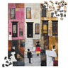 A completed jigsaw puzzle showing an urban street scene of Harlem brownstones with Black women in Sunday white dresses,  plus loose puzzle pieces scattered in the top-right and bottom-left corners on a white background.