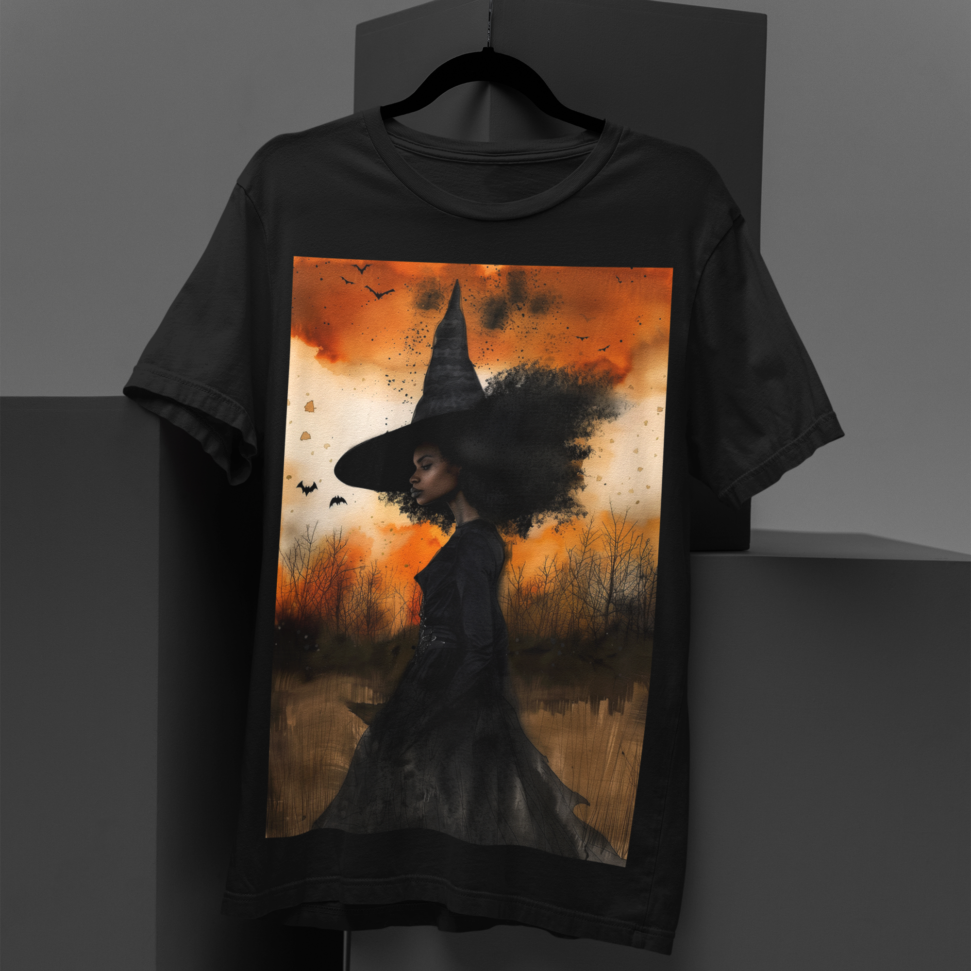Afrocentric Black Witch T-Shirt featuring a watercolor illustration of an African American witch with black bats flying across a dark moody background. Unisex Halloween graphic tee with Afrocentric gothic design.