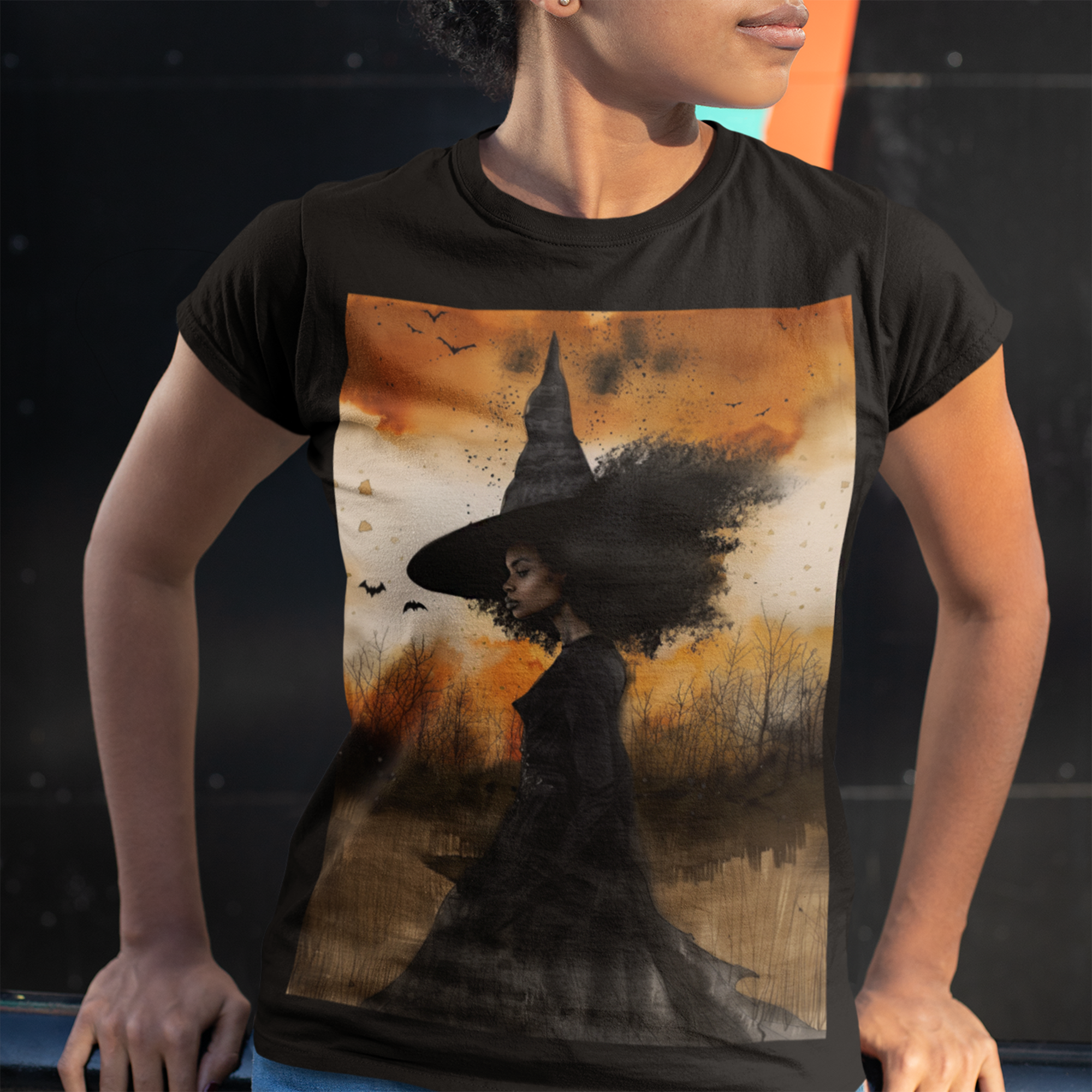 Afrocentric Black Witch T-Shirt featuring a watercolor illustration of an African American witch with black bats flying across a dark moody background. Unisex Halloween graphic tee with Afrocentric gothic design.