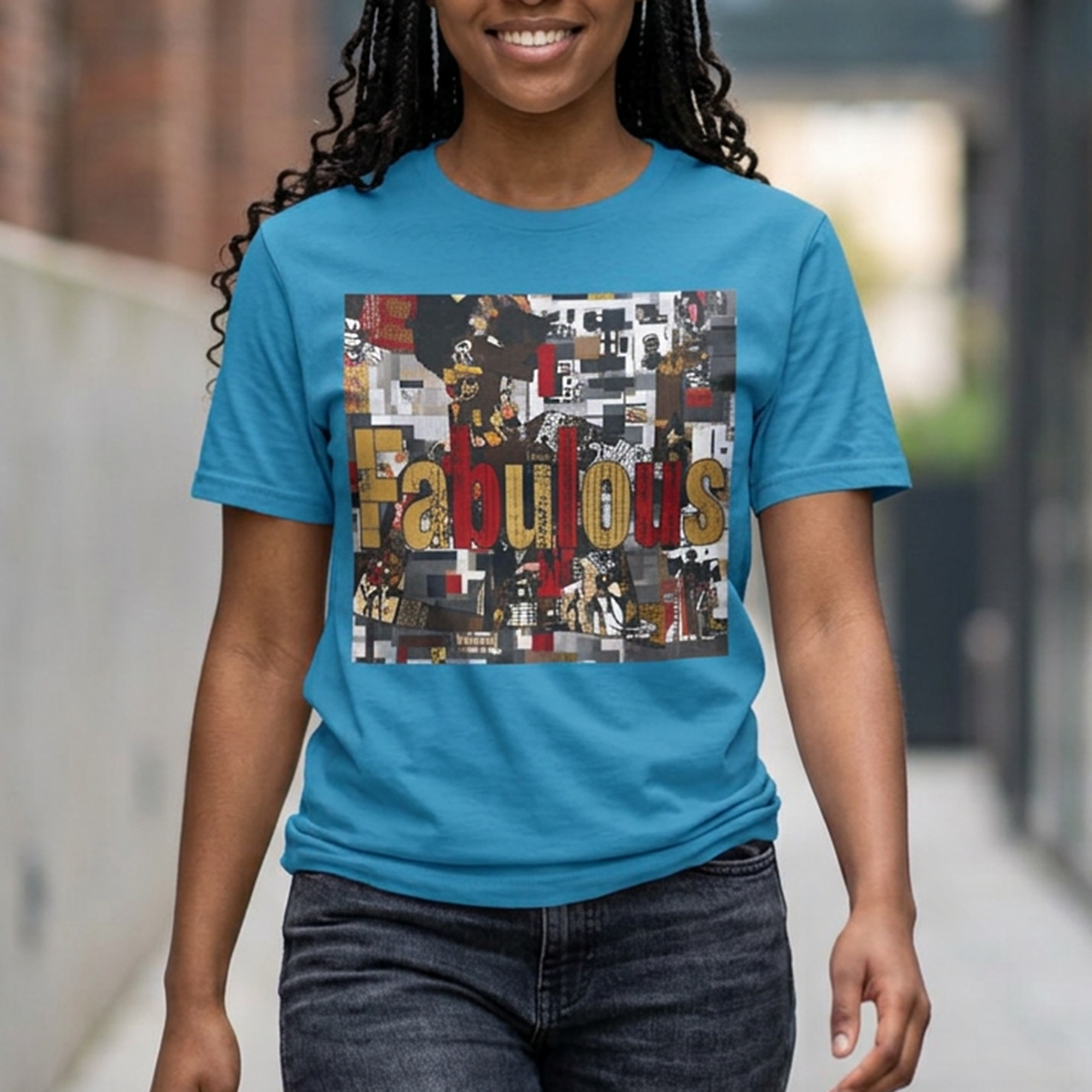 A woman wearing a bright blue crewneck t-shirt with a large graphic print on the front that reads 'Fabulous' in gold letters over a collage of images featuring a stylized Black female. The background is a blurred outdoor walkway.