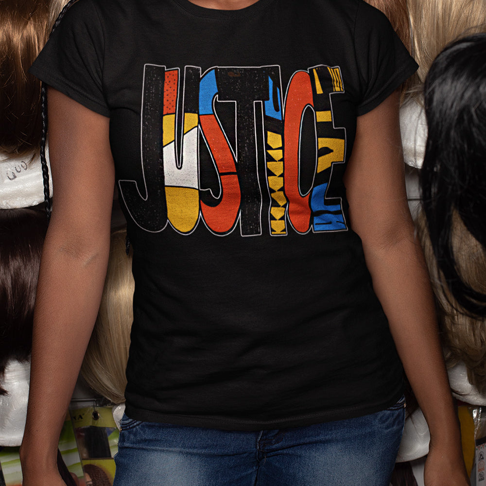 A woman wearing a black graphic t-shirt with the word 'JUSTICE' filled with colorful patterns, paired with blue jeans. 