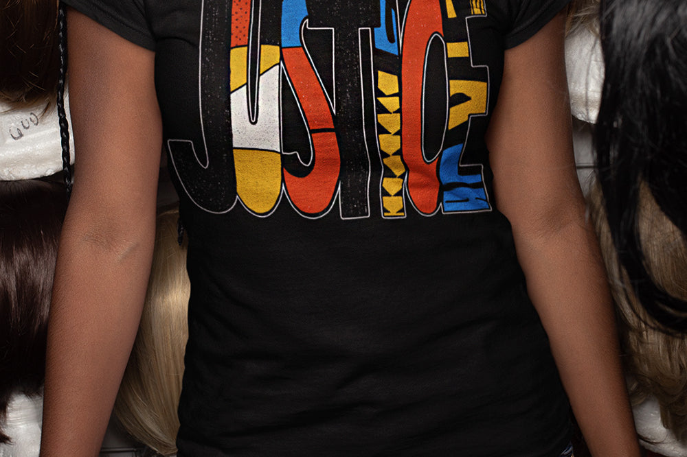 A woman wearing a black graphic t-shirt with the word 'JUSTICE' filled with colorful patterns, paired with blue jeans. 
