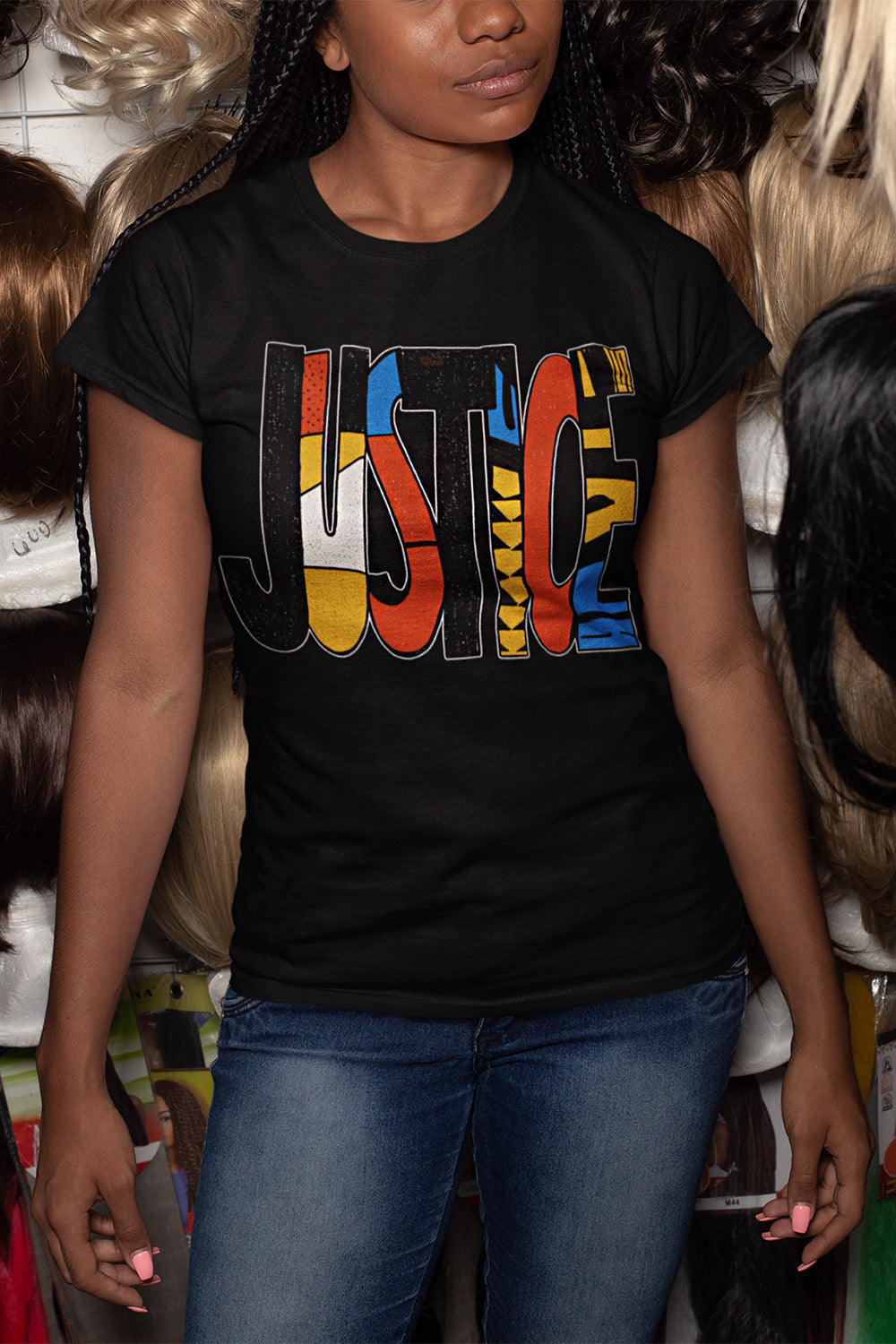 A woman wearing a black graphic t-shirt with the word 'JUSTICE' filled with colorful patterns, paired with blue jeans. 