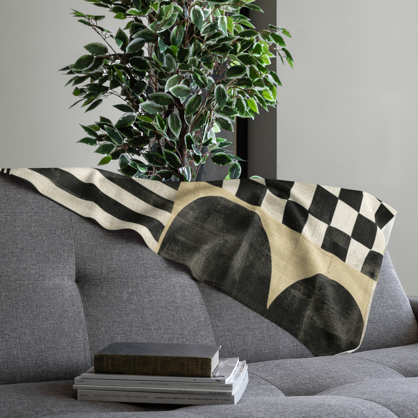 Folded view of Afrocentric geometric art throw blanket featuring bold black, red, gold, cream, and neutral abstract patterns with circles, spirals, grids, and textured African-inspired geometric shapes, draped over the end of a grey sofa.