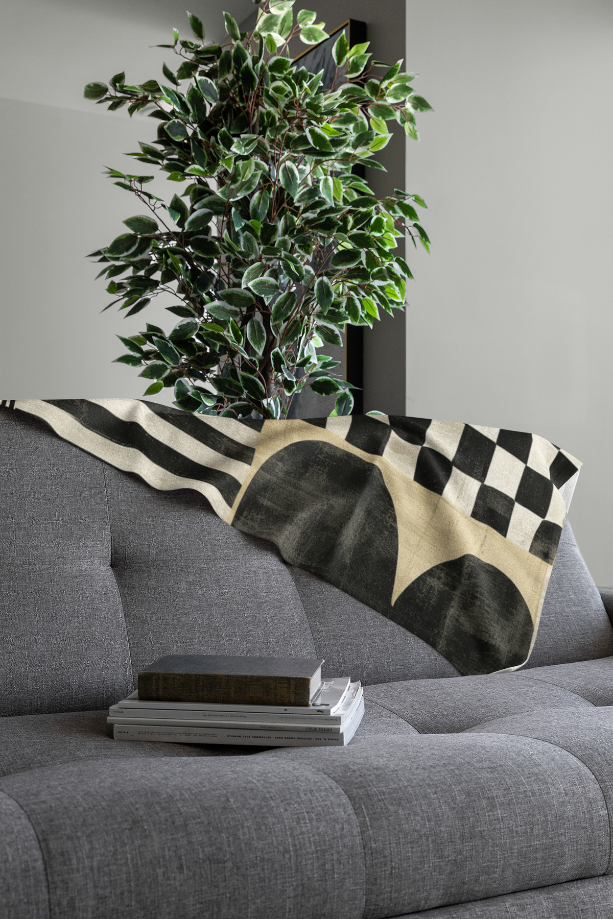 Folded view of Afrocentric geometric art throw blanket featuring bold black, red, gold, cream, and neutral abstract patterns with circles, spirals, grids, and textured African-inspired geometric shapes, draped over the end of a grey sofa.