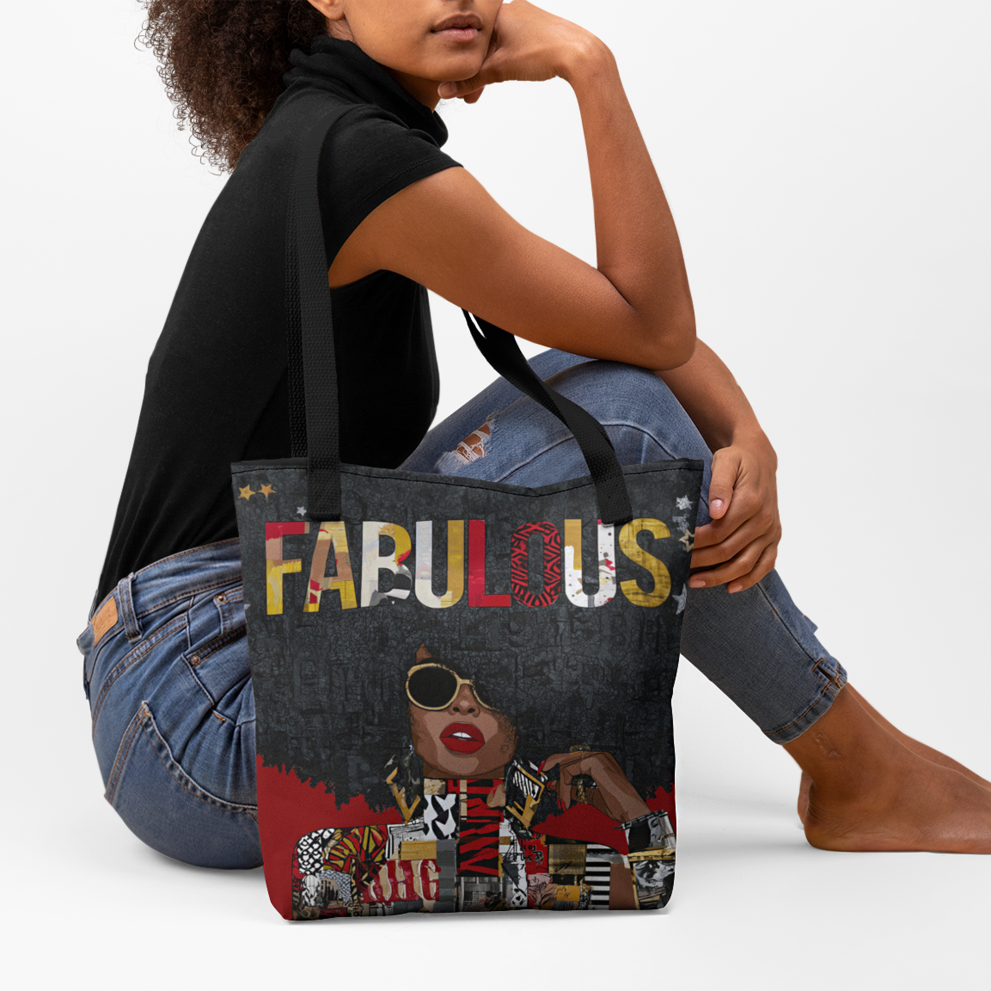 A model sitting on the from with theFabulous Black woman tote bag featuring an abstract Afrocentric female portrait in colorful pop art and graffiti style with the word Fabulous in large graphic letters, hanging from the edge of a board.  Placed against a white background.