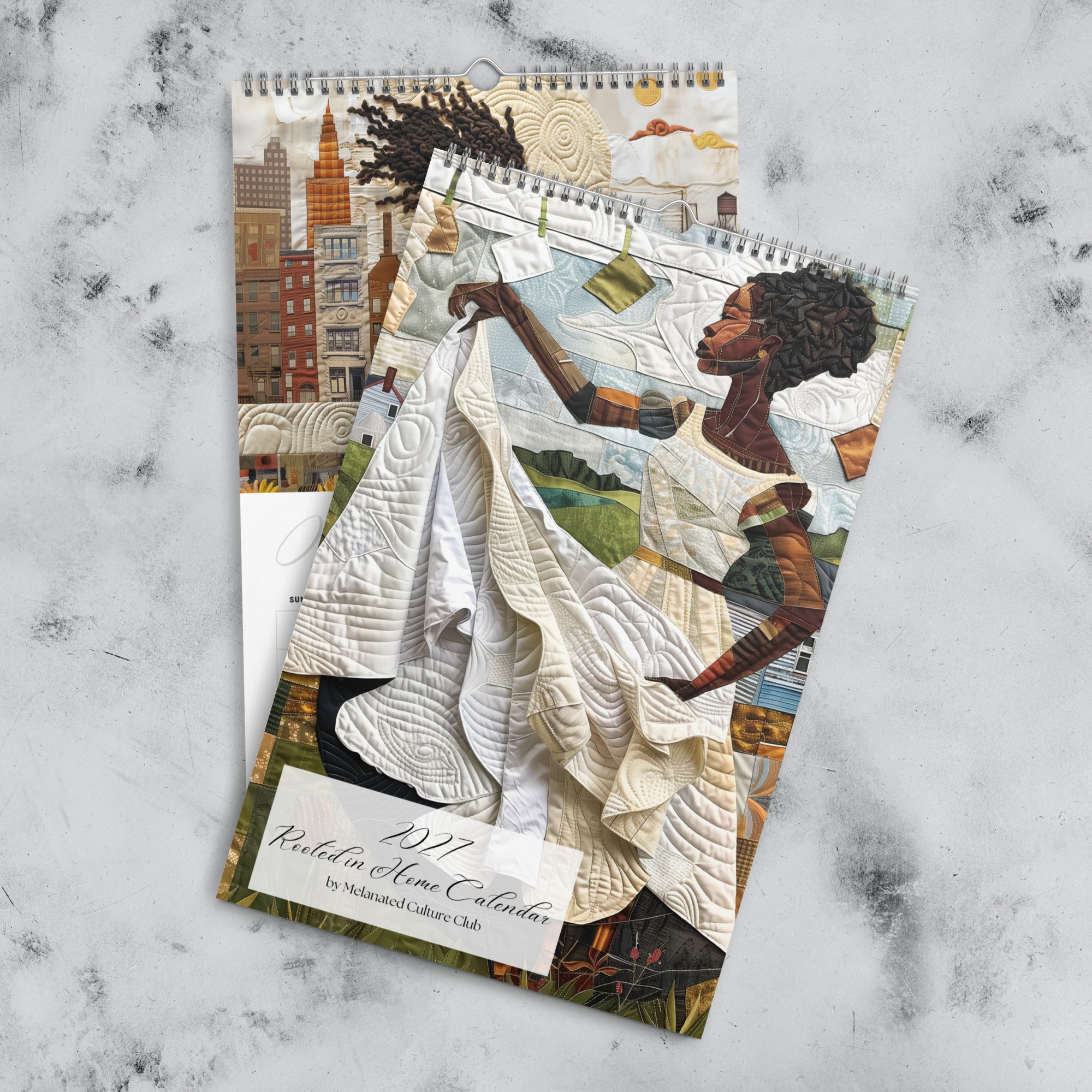 Views of front cover and the month of January of an 11" x 17" 2027 Rooted in Home Wall Calendar featuring vibrant African American quilt collage artwork celebrating the everyday lives of Black women, displayed against a grey marble background.